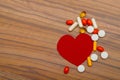 Red heart and many bright pills drugs on wooden background.