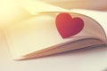 Red heart near the book, light background, sunny flare. The concept of love. Valentine`s Day. Vintage Royalty Free Stock Photo