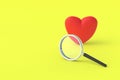 Red heart near magnifier on yellow background