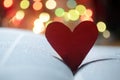 Red heart on an open book page with colorful bokeh lights background. Copy space.