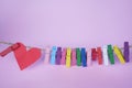 Red heart and colorful paper clips on rope on soft pink purple background.