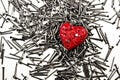 Red heart on pile of iron nails, pierced by a nail and holes in Royalty Free Stock Photo