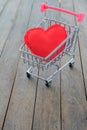 A red heart pillow in mini shopping cart on wooden table. Royalty Free Stock Photo