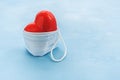 Red heart protected by a medical mask on a blue background. Royalty Free Stock Photo