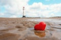 red heart in sand at coast against lighthouse. Fall in love with holiday at seaside concept