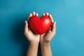 Adult hands holding red heart on light blue background