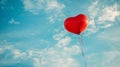 A red heart shaped balloon flying in the sky with a blue cloudy background, AI