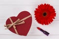 Red heart shaped box, lipstic and daisy flower.