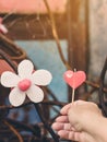A red heart-shaped candle on woman`s hand and an artificial flower made of white and red candles with bluerd image of rusty steel