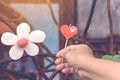 A red heart-shaped candle on woman`s hand and an artificial flower made of white and red candles with bluerd image of rusty steel