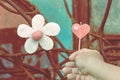 A red heart-shaped candle on woman`s hand and an artificial flower made of white and red candles with bluerd image of rusty steel