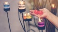 A red heart shaped candle in a woman`s hand with candlelight in many small glass cups.