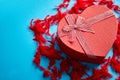 Red, heart shaped gift box placed on blue background among red feathers Royalty Free Stock Photo