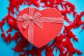 Red, heart shaped gift box placed on blue background among red feathers Royalty Free Stock Photo
