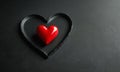 red heart-shaped object rests on black surface, contrasting with the dark background. Royalty Free Stock Photo