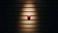 Red heart shaped object on a slatted surface highlighted by a spotlight in a dark setting Royalty Free Stock Photo