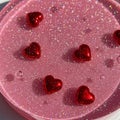 Red heart-shaped objects rest on a pink, glittery surface. The surface has a glossy Royalty Free Stock Photo
