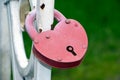 Red heart-shaped padlock hanging on a metal white fence on green background Royalty Free Stock Photo