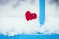 Red heart in snow by blue fence