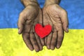 Red heart in soldier hands on the blue and yellow National flag of Ukraine background