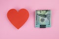 Red heart and a stack of hundred-dollar bills held together with a metal clip on a pink background Royalty Free Stock Photo