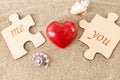 Red heart and two pieces of wooden puzzle, on sandy background with seashells. Royalty Free Stock Photo