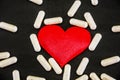 Red heart and white capsules on a black background. Health concept. Royalty Free Stock Photo