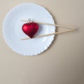 A red heart on a white plate and Chinese sticks on beige background. Minimal love scene