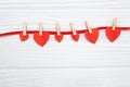 Red hearts with clothespins hanging on clothesline on white wooden background