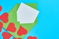 Red hearts near open green postal envelope with blank white paper on blue desk. Love message Royalty Free Stock Photo