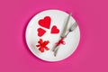 Red hearts on a white plate  a fork  a knife  a gift box on a pink background  top view  copy space. Valentine`s day Royalty Free Stock Photo