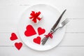 Red hearts on a white plate  a fork  a knife  a red ribbon  a gift box on a white wooden table  top view  space for text. Wedding Royalty Free Stock Photo