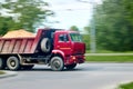 Red heavy industrial dump truck lorry with sand in back, panning blur shot moving in city motion blur over green foliage blurred Royalty Free Stock Photo