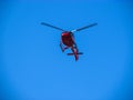 A red helicopter flies across the sunny blue sky