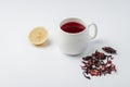 red hibiscus tea in a white mug, lemon segment and dry blossom isolated on white background