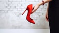 Red high heels shoes kept in hands. A woman holds in her hands high-heeled shoes, red color, on a white brick background, Royalty Free Stock Photo