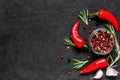 Red hot chili peppeprs and peppercorns with rosemary and garlic on black stone background