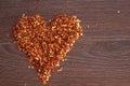 Red hot chili pepper flakes lying on wooden table in heart shape. Cooking concept, seasonings for food. Royalty Free Stock Photo