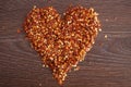 Red hot chili pepper flakes lying on wooden table in heart shape. Cooking concept, seasonings for food. Royalty Free Stock Photo