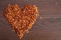 Red hot chili pepper flakes lying on wooden table in heart shape. Cooking concept, seasonings for food. Royalty Free Stock Photo