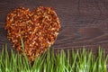 Red hot chili pepper flakes lying on wooden table in heart shape with green grass. Cooking concept, seasonings for food. Royalty Free Stock Photo