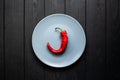 Red hot chili pepper on a gray matte plate that stands on a black wooden background Royalty Free Stock Photo