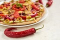 Red hot chili pepper on white surface close up. On blurred background vegetarian pizza with tomatoes, bell pepper, onion Royalty Free Stock Photo