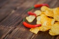 Red hot chili peppers and potato chips lie on a wooden table made of pine boards. Daylight. Close-up. Royalty Free Stock Photo