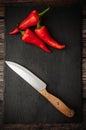 Red hot chili peppers on a slate cutting board on a dark wooden table with a knife. Top down overhead view