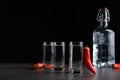Red hot chili peppers and vodka on grey table against black background, space for text Royalty Free Stock Photo