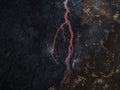 Red hot lava flow streaming over black volcanic rocks, aerial directly above