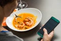 Red hot spicy prawn soup with woman hand and cellphone