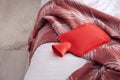 Red hot water bottle on bed indoors Royalty Free Stock Photo