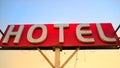 Red hotel sign on top of a dirty old motel on blue sky background. Old unclean hotel facade with vintage neon sign retro